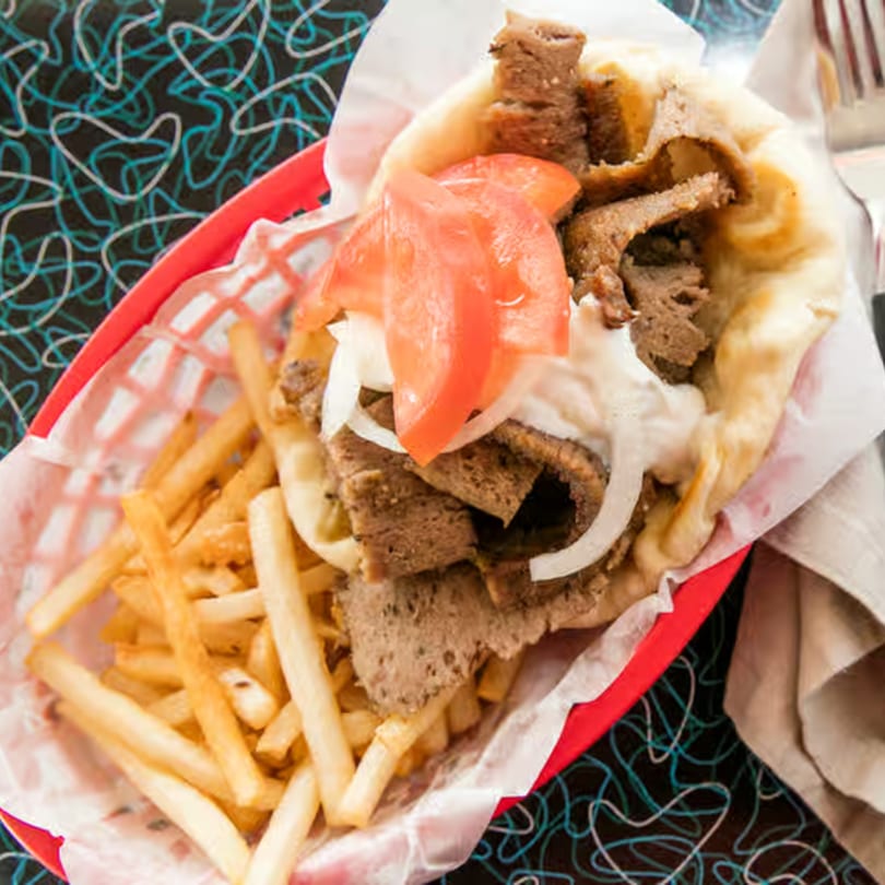 A Bo-Bo's Gyros pita with meat, tomatoes, onions, and sauce, served with fries in a red basket.