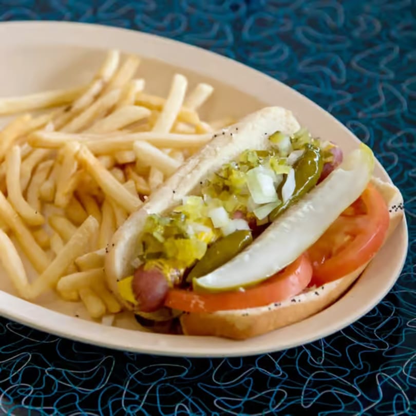 A Bo-Bo's Gyros hot dog with fries, topped with relish, onions, tomato, and a pickle spear.