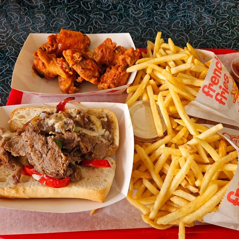 A Bo-Bo's Gyros diner meal with a cheesesteak, buffalo wings, and french fries.