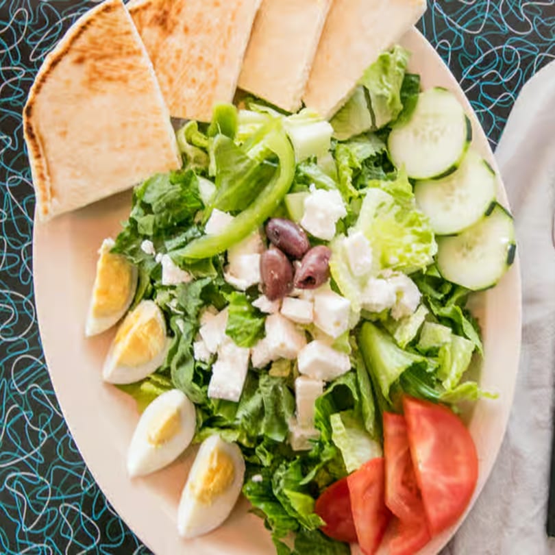 A fresh Greek salad with pita bread, lettuce, tomatoes, cucumbers, olives, feta, and hard-boiled eggs.