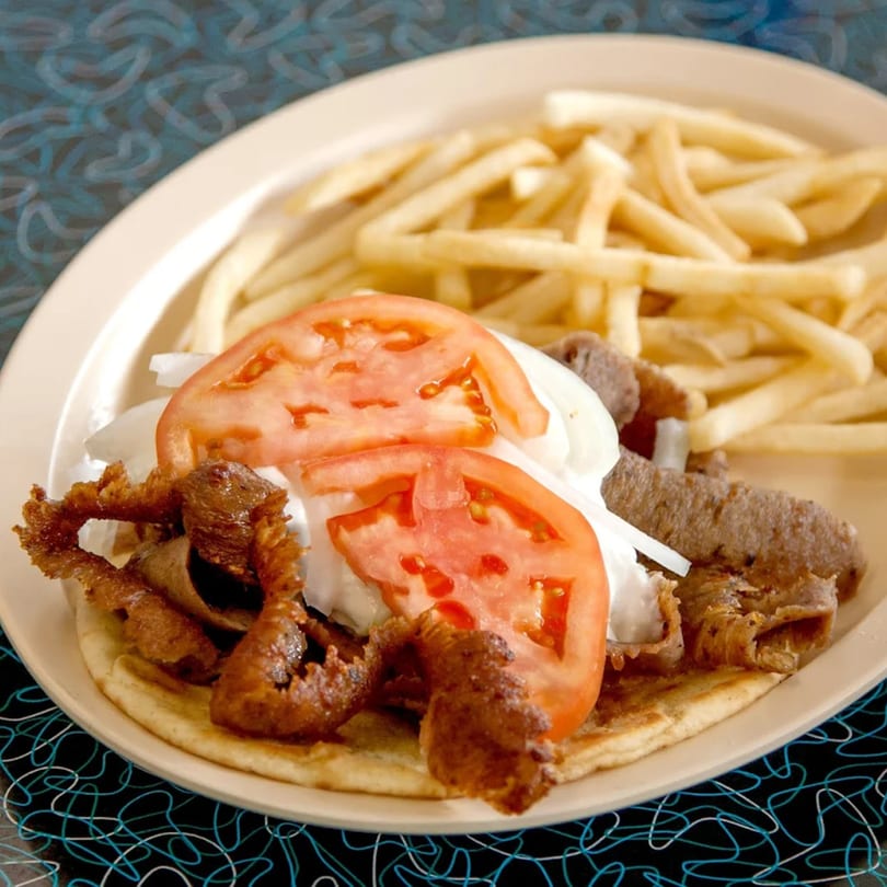 A Bo-Bo's Gyros plate with meat, tomatoes, onions, tzatziki, and a side of fries.